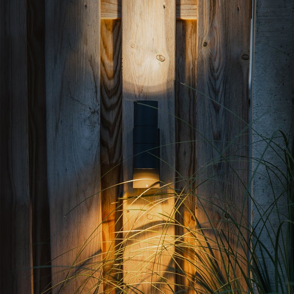 Moderne Außenwandleuchte an einem Holzzaun montiert, strahlt Licht nach oben und unten auf die Holzplanken.