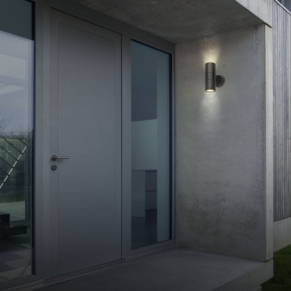 Moderne Hauseingangsszene mit zylindrischer Außenwandleuchte an einer Betonwand, die Licht nach oben und unten strahlt.