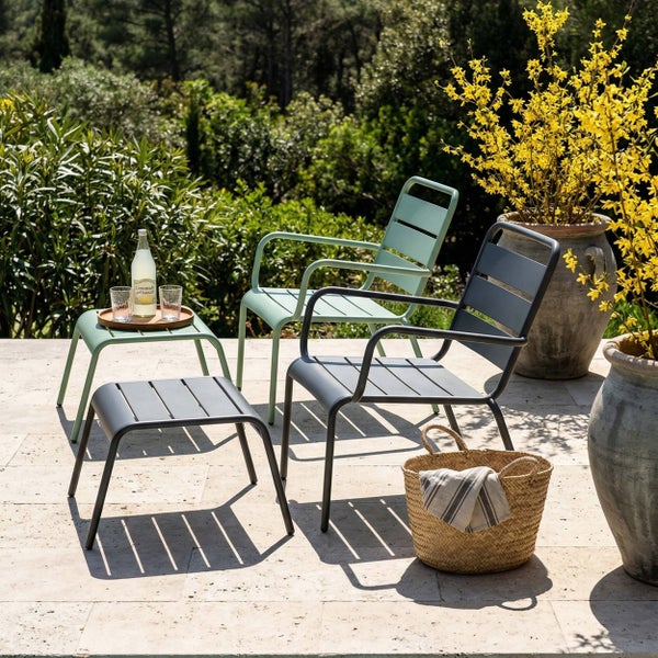 Moderne Garten-Armlehnenstühle und Hocker aus Metall auf einer hellen, organisierten Steinterrasse im Garten.