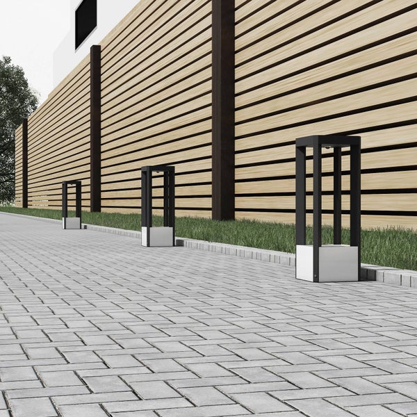 Drei moderne Außenstandleuchten mit schwarzem Rahmen und weißem Sockel an einem gepflasterten Weg neben einem Holzzaun.