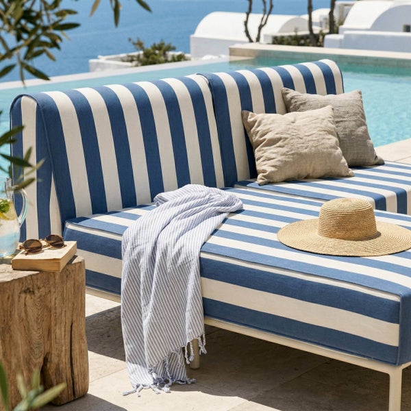 Modernes blau-weiß gestreiftes Outdoor-Lounge-Sofa auf einer hellen Terrasse am Pool mit Kissen, Decke und Strohhut.