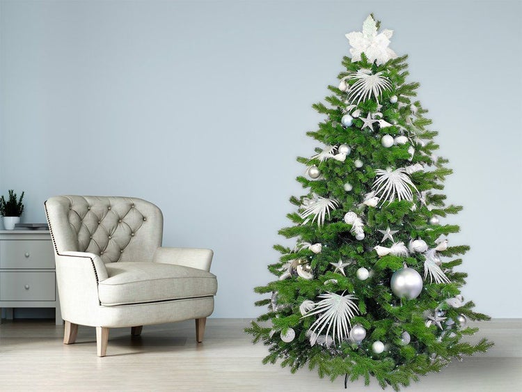 Geschmückter künstlicher Weihnachtsbaum in einem Wohnzimmer neben einem Sessel mit weißer Weihnachtsdekoration und Sternen als Baumschmuck