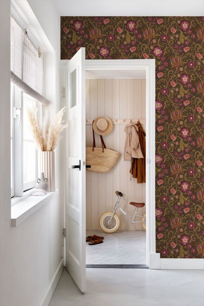 Heller Flur mit floraler Mustertapete an der Wand und Blick durch eine offene weiße Tür in einen Eingangsbereich mit Holzpaneelen.