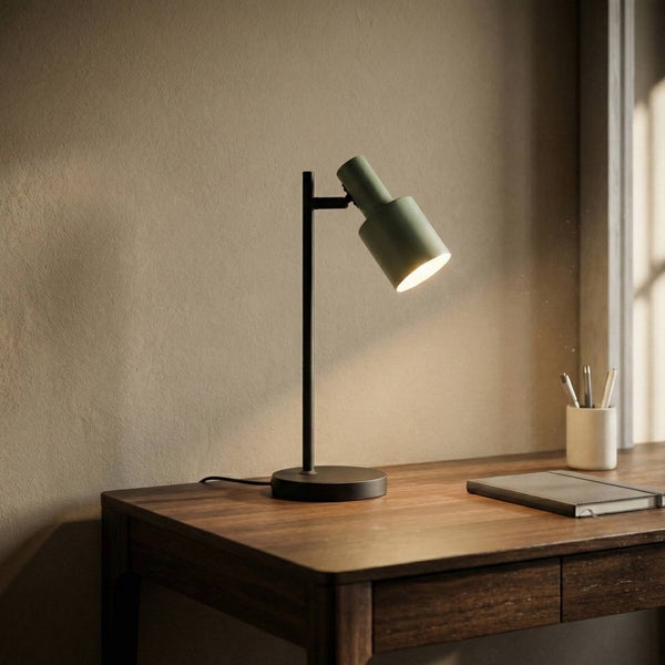 Schreibtisch mit einer grünen Tischleuchte, einem Notizbuch und Stiften.