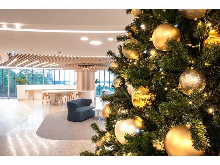 Weihnachtsbaum mit goldener Dekoration und Lichterkette in einer modernen Bürolounge mit Lounge Möbeln und großflächiger Fensterfront.