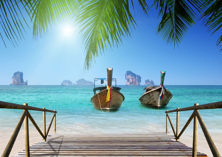 Szene mit zwei traditionellen thailändischen Booten im Meer, gesehen von einem Holzsteg aus.