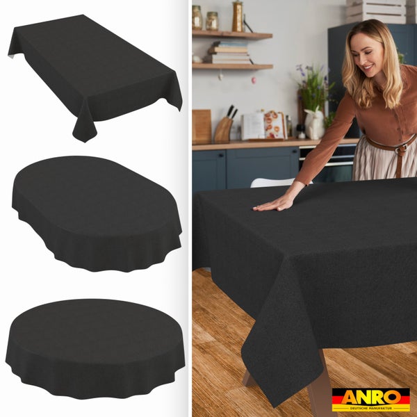 Anthrazitfarbene Tischdecke in rechteckiger, ovaler und runder Form. Eine Frau legt die Decke in einer Küche auf einen Holztisch. ANRO Logo.
