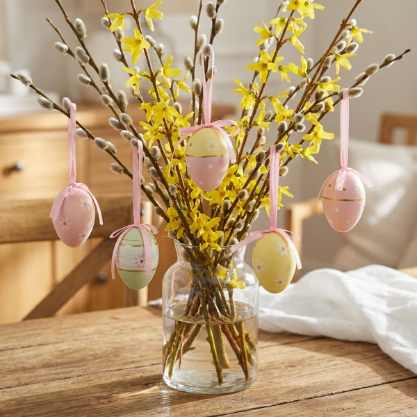 Osterstrauß mit Weidenkätzchen und Forsythien in Glasvase mit hängenden Ostereiern als Frühlingsdekoration auf einem Holztisch