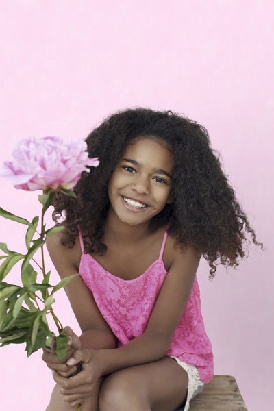 Ein junges Mädchen lächelt und hält eine Pfingstrose in ihren Händen.