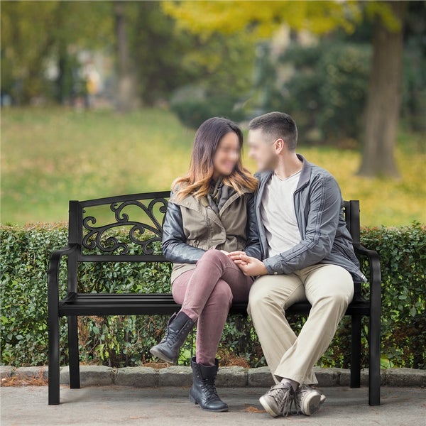 Paar sitzt auf einer schwarzen Gartenbank mit Metallgestell und verzierter Rückenlehne