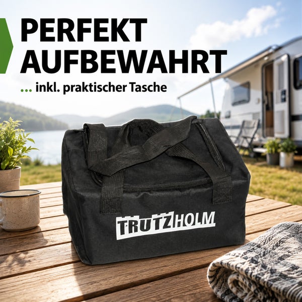 Schwarze Trutzholm Tragetasche für Campingzubehör auf einem Holztisch im Außenbereich vor einem Wohnmobil und einem See.
