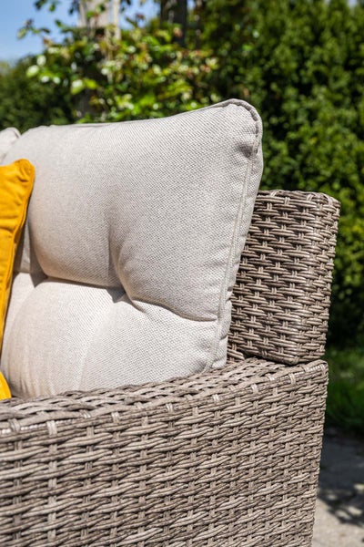Detailansicht eines Gartenmöbels aus grauem Polyrattan-Geflecht mit einem hellen Rückenkissen und einem gelben Zierkissen.