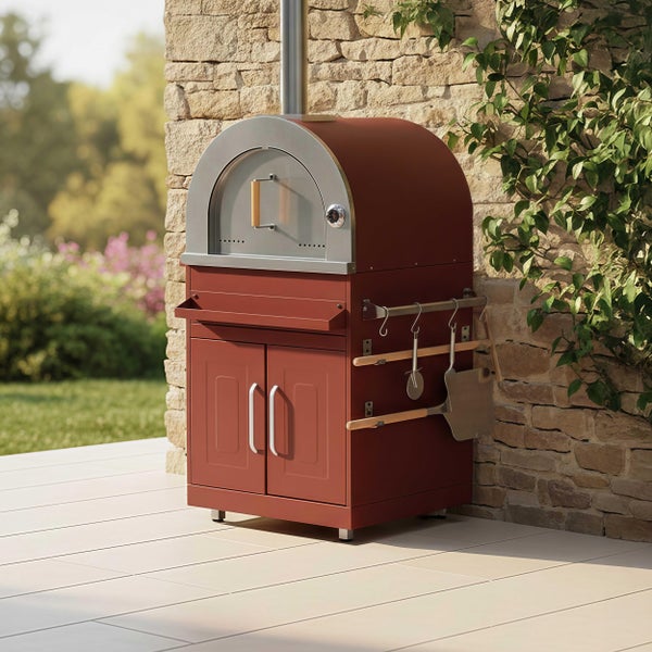 Freistehender Pizzaofen mit Unterschrank und Zubehörhaltern auf einer Terrasse an einer Natursteinmauer.