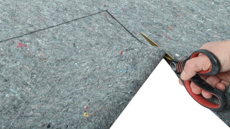 Hand führt eine Schere beim Zuschneiden von grauem Abdeckvlies entlang einer markierten Linie.