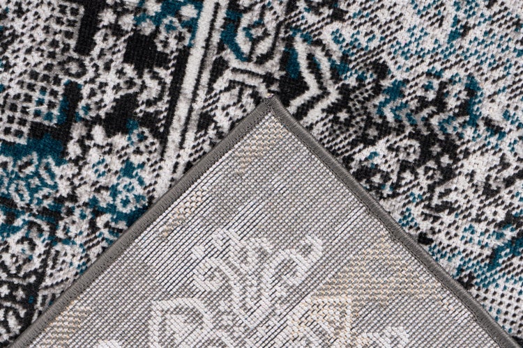 Detailaufnahme eines Teppichs mit schwarz-weißem und türkisem Muster, umgeschlagene Ecke zeigt die Rückseite und die graue Kettelung.