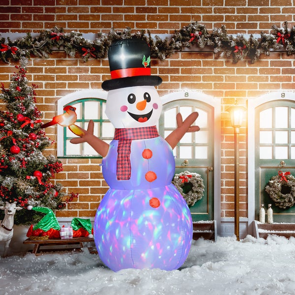 Aufblasbarer Schneemann mit bunter Beleuchtung, Zylinder und Schal in einer weihnachtlichen Szene mit Weihnachtsbaum vor einer Backsteinwand.