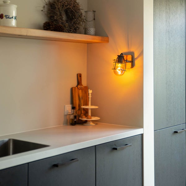 Moderne Küche mit dunklen Schränken, heller Arbeitsplatte und einer Wandleuchte mit Filamentlampe im Vintage Stil.