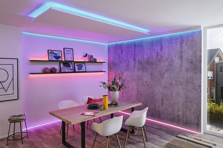 Moderner, heller Essraum mit Holztisch, Stühlen und smarter LED-Streifen-Beleuchtung an Decke, Boden und Regalen vor einer Wand in Betonoptik.