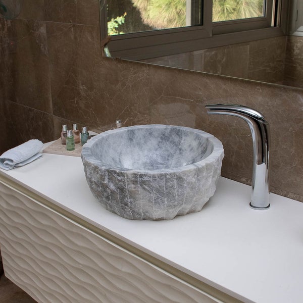 Modernes Badezimmer mit einem runden Aufsatzwaschbecken aus grauem Naturstein auf einem weißen Waschtisch und einer verchromten Armatur.
