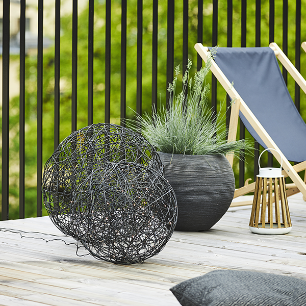 Terrassenszene mit Kugelleuchten, Pflanzgefäß, Windlicht und Liegestuhl