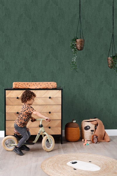 Kinderzimmer mit Kommode, Laufrad, Spielzeug und grüner Blättertapete