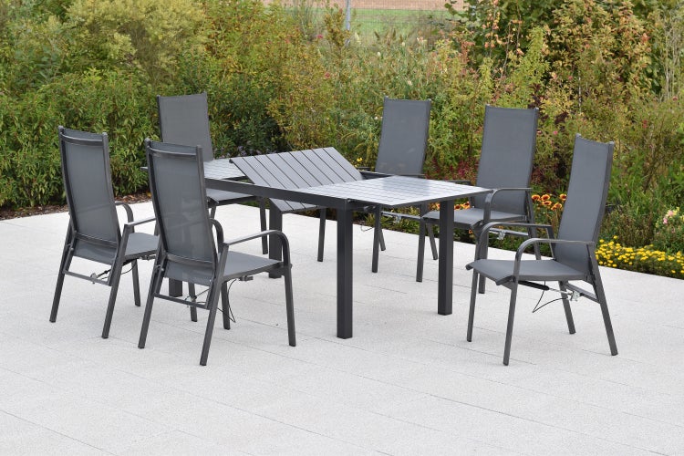 Gartenmöbel-Set mit ausziehbarem rechteckigem Tisch mit Lattenplatte und sechs Hochlehner-Stühlen auf einer gepflasterten Terrasse im Garten.