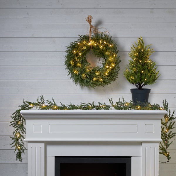 Weihnachtsdekoration mit Kranz, Girlande und kleinem Baum auf einem Kamin