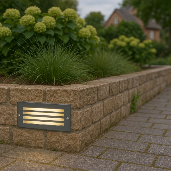 Rechteckige LED-Wandeinbauleuchte in einer Natursteinmauer zur Gartenbeleuchtung an einem gepflasterten Weg.