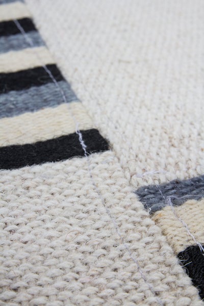 Detailaufnahme eines gewebten Teppichs mit Streifenmuster und einer groben, strukturierten Oberfläche.