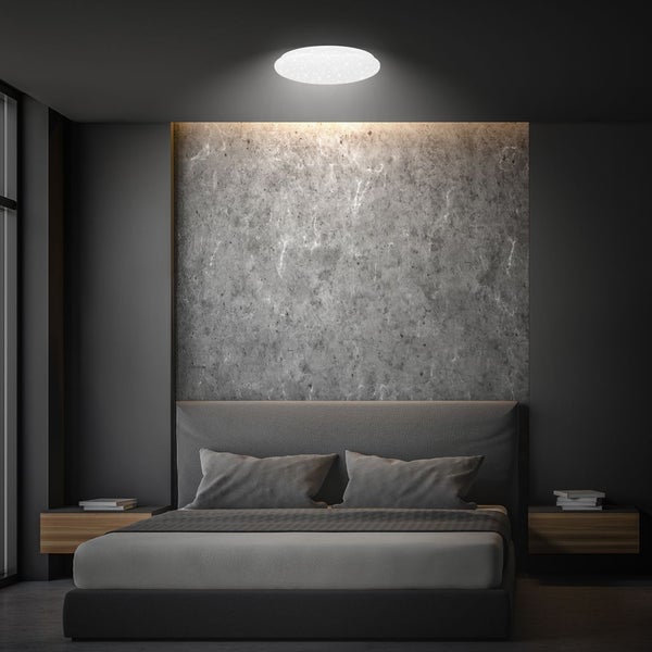 Runde LED-Deckenleuchte in einem modernen Schlafzimmer mit Wand in Betonoptik und grauem Polsterbett.
