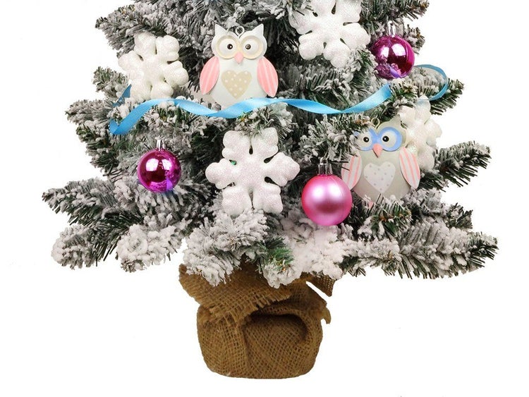 Künstlicher Weihnachtsbaum, verschneit, dekoriert mit Eulen, Schneeflocken und Weihnachtskugeln, in einem Jutesack stehend.