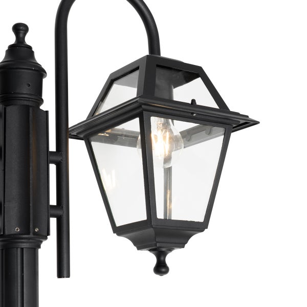 Schwarze Außenwandleuchte in Laternenform aus Metall und Glas mit sichtbarem Leuchtmittel.