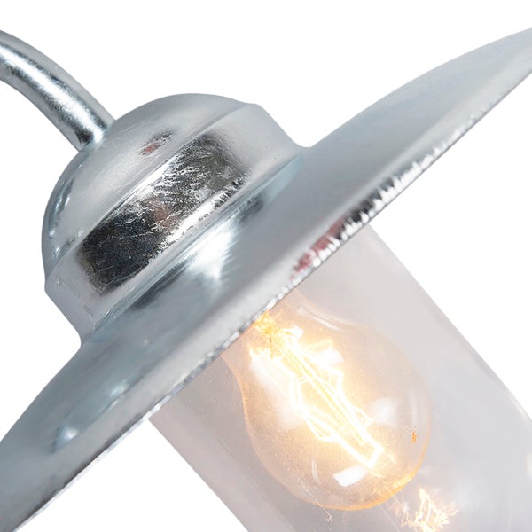 Nahaufnahme einer industriellen Außenwandleuchte mit verzinkter Metalloberfläche, klarem Glaszylinder und leuchtendem Filament-Leuchtmittel.