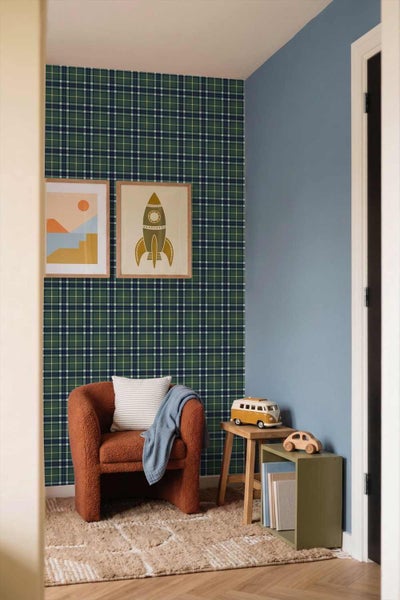 Ein Kinderzimmer mit karierter Vliestapete an der Wand, einem braunen Sessel, Wandbildern mit Raketenmotiv und einem hellen Teppich.