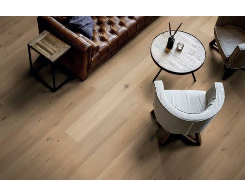 Heller Parkettboden in einem Wohnzimmer mit einem braunen Ledersofa, einem runden Couchtisch aus Holz und einem hellen Sessel.