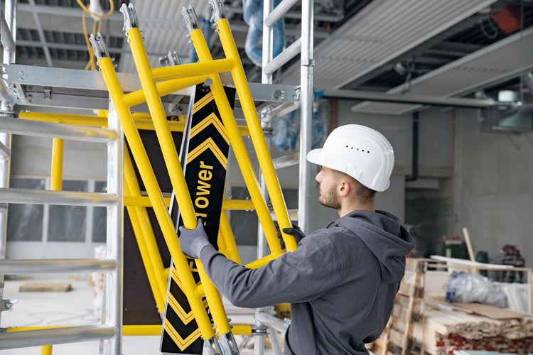 Mann mit Schutzhelm montiert Baugerüst auf einer Baustelle.