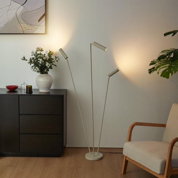 Moderne Stehleuchte mit drei verstellbaren Strahlern in einem minimalistischen Wohnzimmer mit dunklem Sideboard und Sessel.