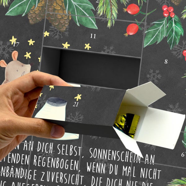 Hand zieht eine geöffnete Schachtel mit der Nummer einundzwanzig aus einem Adventskalender, die eine kleine Süßigkeit enthält.