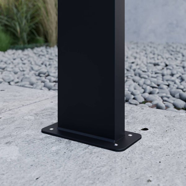 Detailansicht eines schwarzen rechteckigen Pfostenfußes, der mit Schrauben auf einer Betonoberfläche montiert ist.