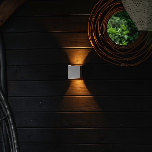 Quadratische LED-Außenwandleuchte mit Up-and-Down-Lichteffekt an einer dunklen Holzwand.