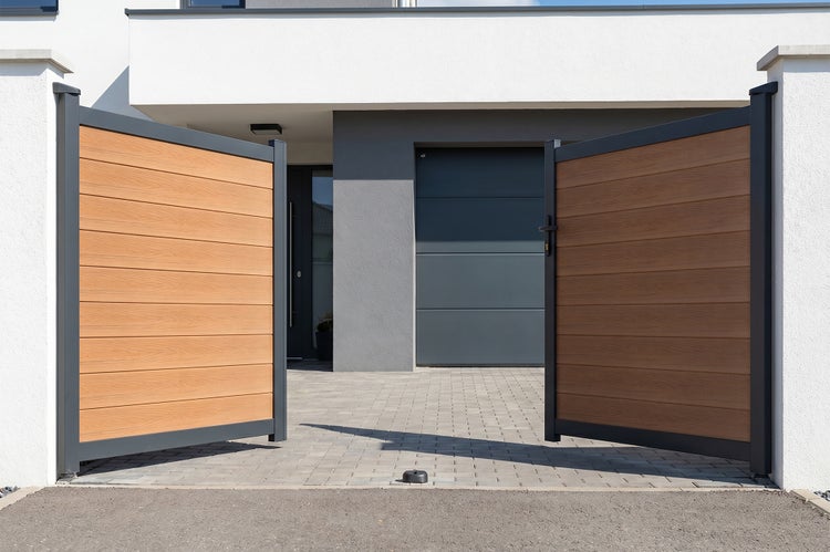 Zweiflügeliges Einfahrtstor mit Aluminiumrahmen und Füllung in Holzoptik vor einem modernen Wohnhaus mit Garage.