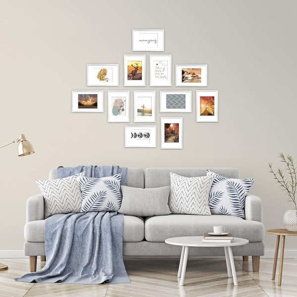 Wohnzimmer mit grauer Couch, Kissen, Decke, Beistelltischen und einer Wand mit Bilderrahmen