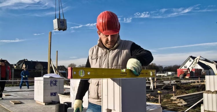 Handwerker mit Schutzhelm verwendet eine Stabila Wasserwaage beim Mauern auf einer Baustelle mit Kalksandsteinen.