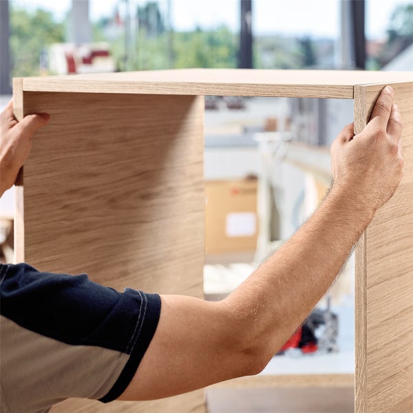 Eine Person montiert ein U-förmiges Holzmöbelelement in Holzoptik.