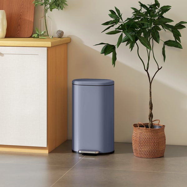 Moderner blauer Tretabfalleimer aus Metall in einer hellen Küche neben einem Holzschrank und einer Zimmerpflanze.