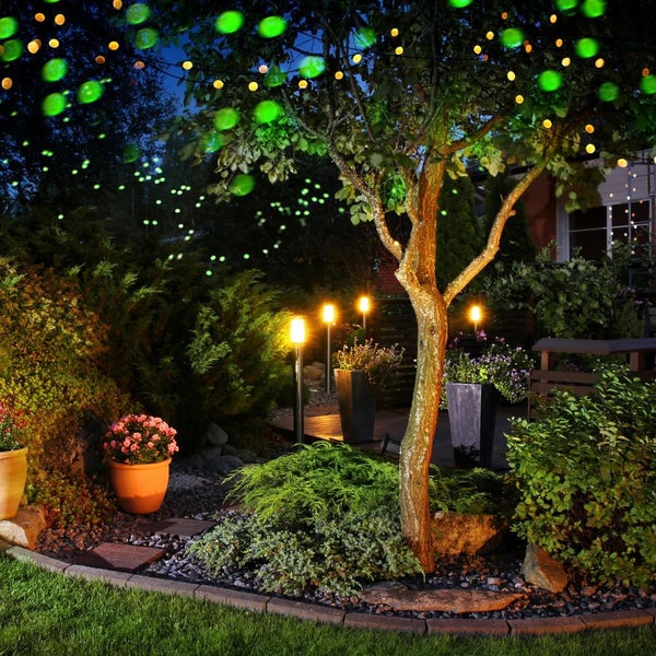 Gartenlandschaft bei Nacht mit Baum, Strauchern, Beetbegrenzungen, Gartenweg, Solarleuchten und Lichterketten