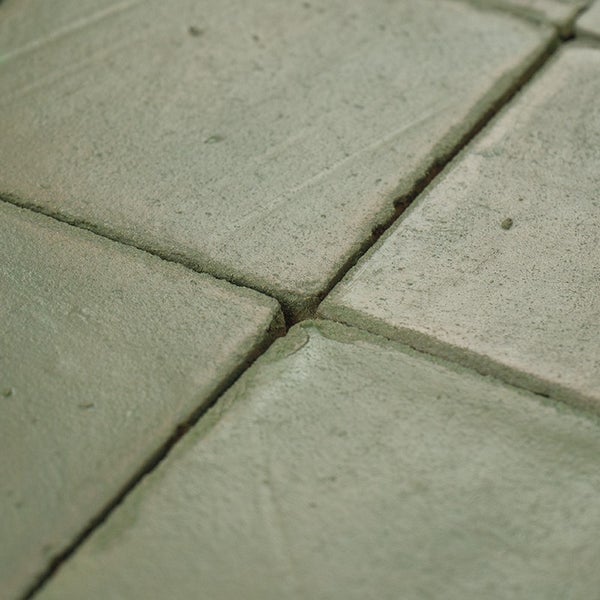 Quadratische Pflastersteine oder Gehwegplatten aus Beton mit rauer Oberflächenstruktur verlegt im Verband.