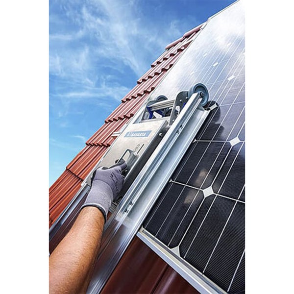 Person verwendet eine Reinigungsmaschine für Photovoltaikanlagen auf einem Ziegeldach mit montierten Solarmodulen.