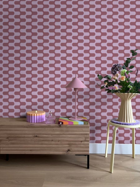 Raumansicht mit Kommode, Lampe, Dekorationen, Blumenstrauß und Stuhl vor einer gemusterten Tapete