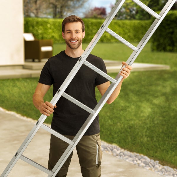 Ein Mann hält eine Aluminiumleiter im Garten.